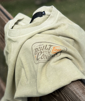 Beige t-shirt with 'Built with Conviction' text on a wooden surface