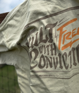 Tan t-shirt with text 'Built with Conviction' on a blurred background – Brand: Free is Life