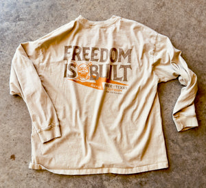 Beige long-sleeve shirt with 'Freedom is Built' text on a textured surface