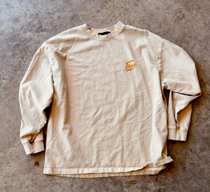 Beige long-sleeve shirt with a logo on a gray concrete surface