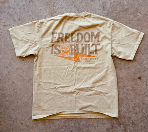 Beige t-shirt with 'Freedom is Built' text on a textured surface