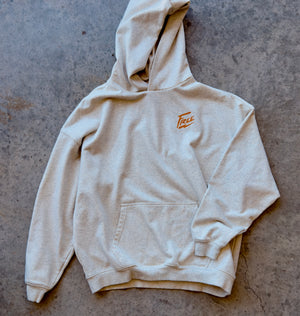 Beige hoodie with a logo on the back, laid flat on a concrete surface
