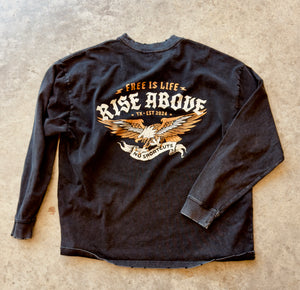 Black long-sleeve shirt with 'Free is Life, Rise Above' design on a beige surface