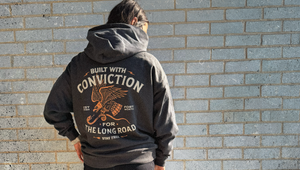 Person wearing a hoodie with text and an eagle design against a brick wall.