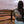 Person wearing a shirt with text standing in front of a wooden fence and open field.