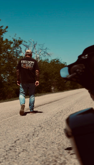Man walking on a road wearing a Freedom is built t-shirt. Brand: Free is Life