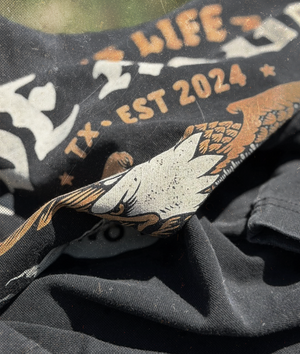 Black shirt with graphic design and the text 'Rise Above' on a grassy background.
