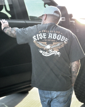 Man wearing a t-shirt with 'Rise Above' design and text, standing next to a vehicle.
