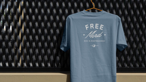 Blue t-shirt with 'Free Mind' text on a textured black wall background